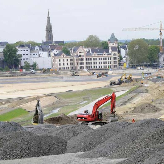 Ansicht eines Baugeländes mit rotem Bagger in Kieshügeln