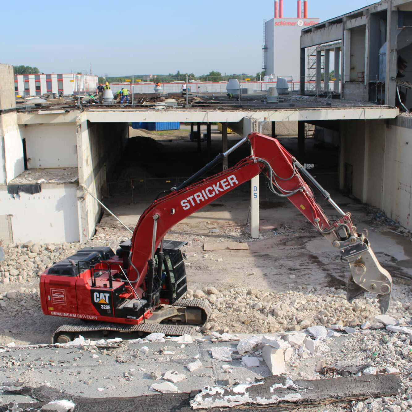 Ein roter Bagger mit dem Stricker Firmenlogo vor einem Abbruchgebäude